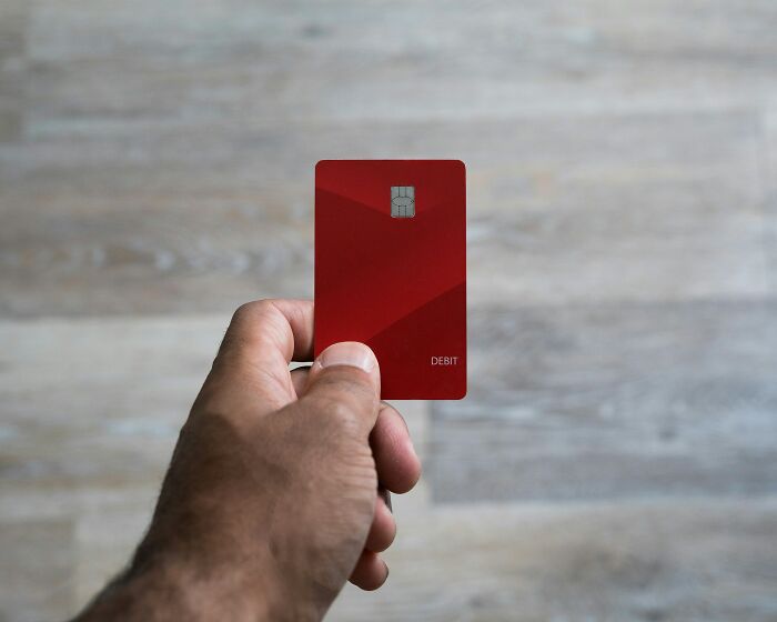 A hand holding a red debit card with a chip, a common sight while visiting the US.