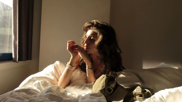 Aesthetic photo of woman sitting on bed in soft morning light by window