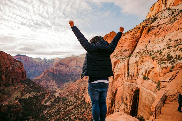 Person celebrating on mountain cliff with raised arms