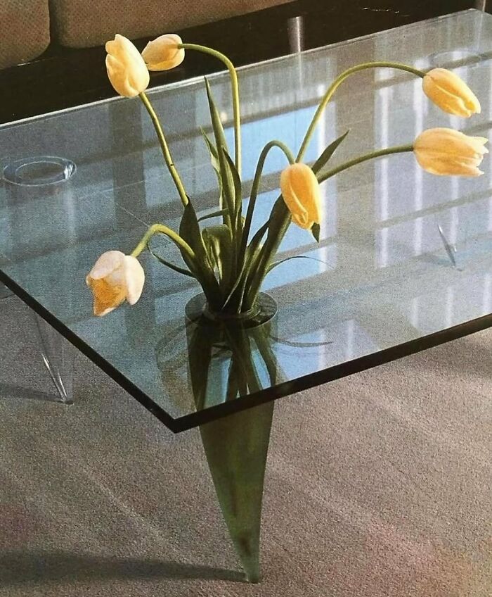 Glass coffee table with green vase holding yellow tulips in a minimalist living room