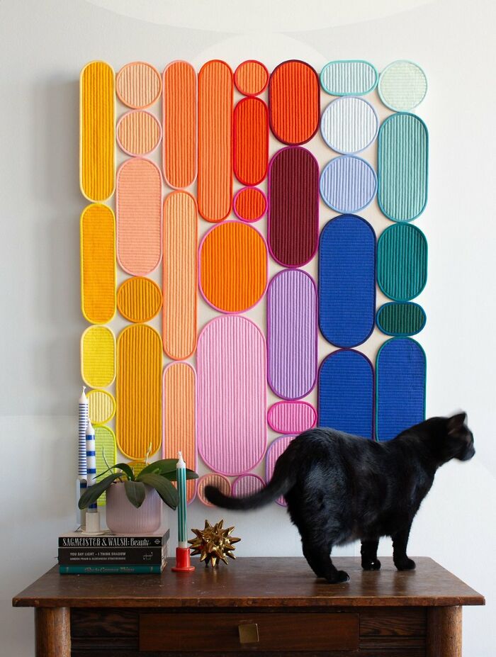 Colorful geometric wall art above wooden table with black cat in interior design