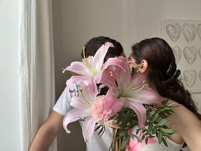 Aesthetic intimate moment with a couple embracing behind a bouquet of pink flowers indoors
