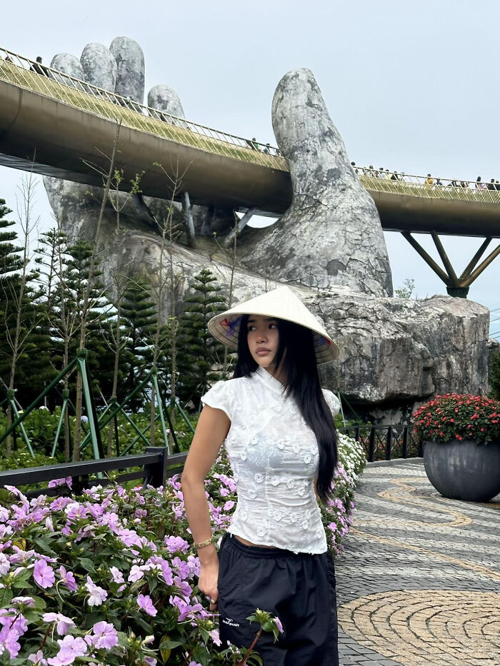 Aesthetic woman wearing a traditional hat standing near the Golden Bridge held by giant stone hands in Vietnam