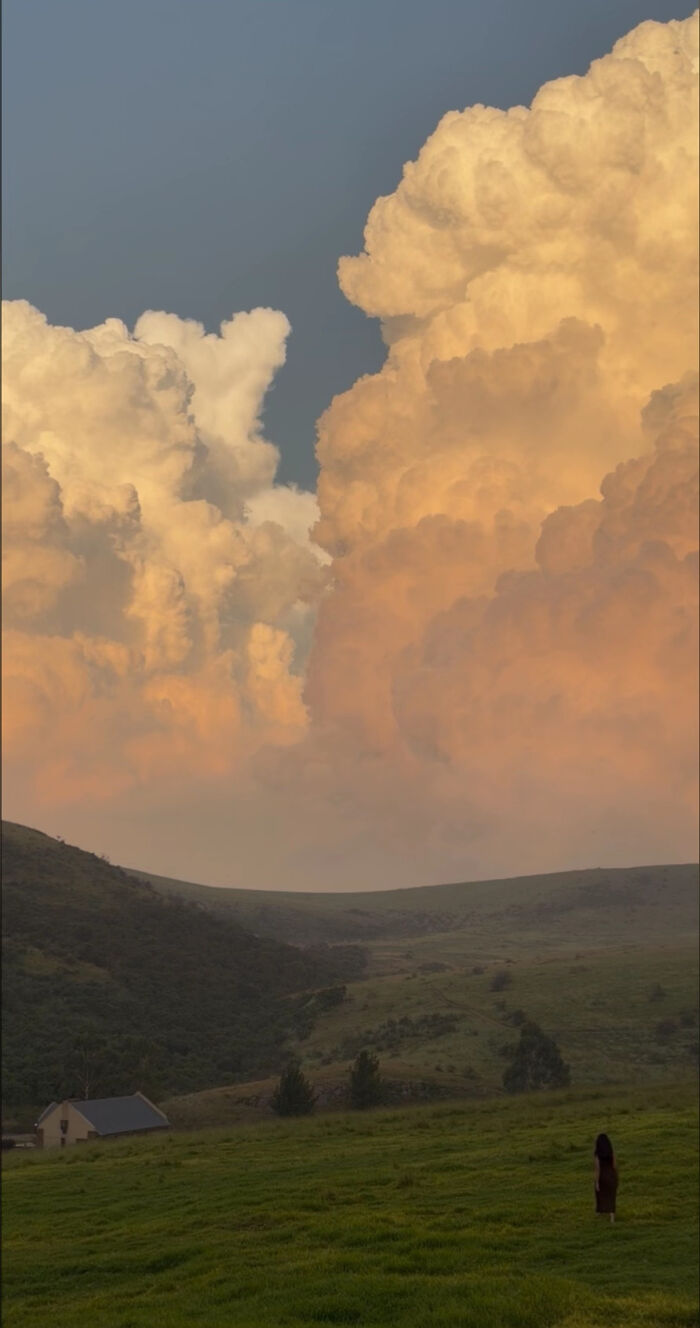Aesthetic sky with dramatic clouds over green hills and solitary figure