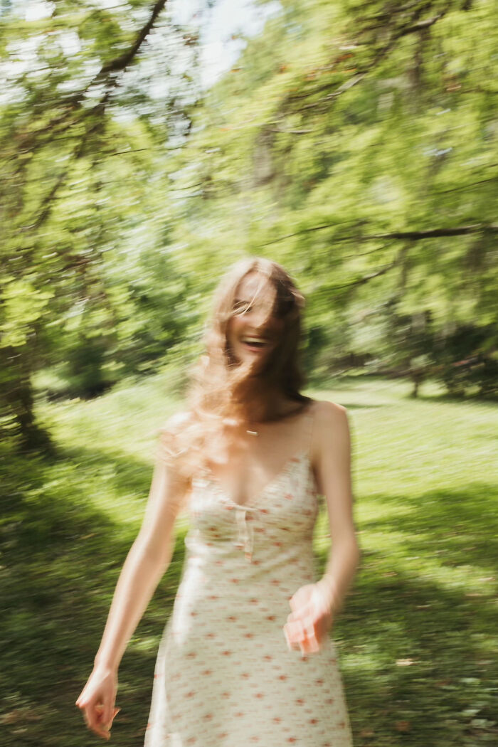 Aesthetic blurred image of smiling woman in floral dress in green forest