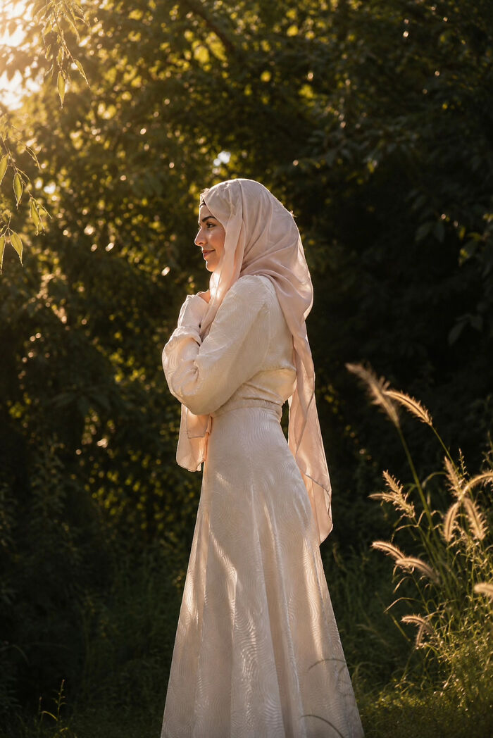Aesthetic portrait of a woman wearing a light pink hijab standing outdoors in golden sunlight