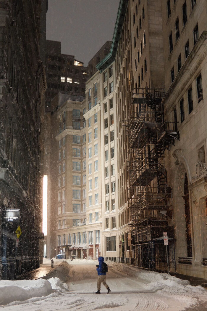 Aesthetic snowy city street with tall buildings and a person walking in the snow