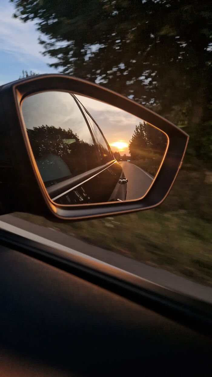 Aesthetic photo of sunset reflected in car side mirror on a tree-lined road