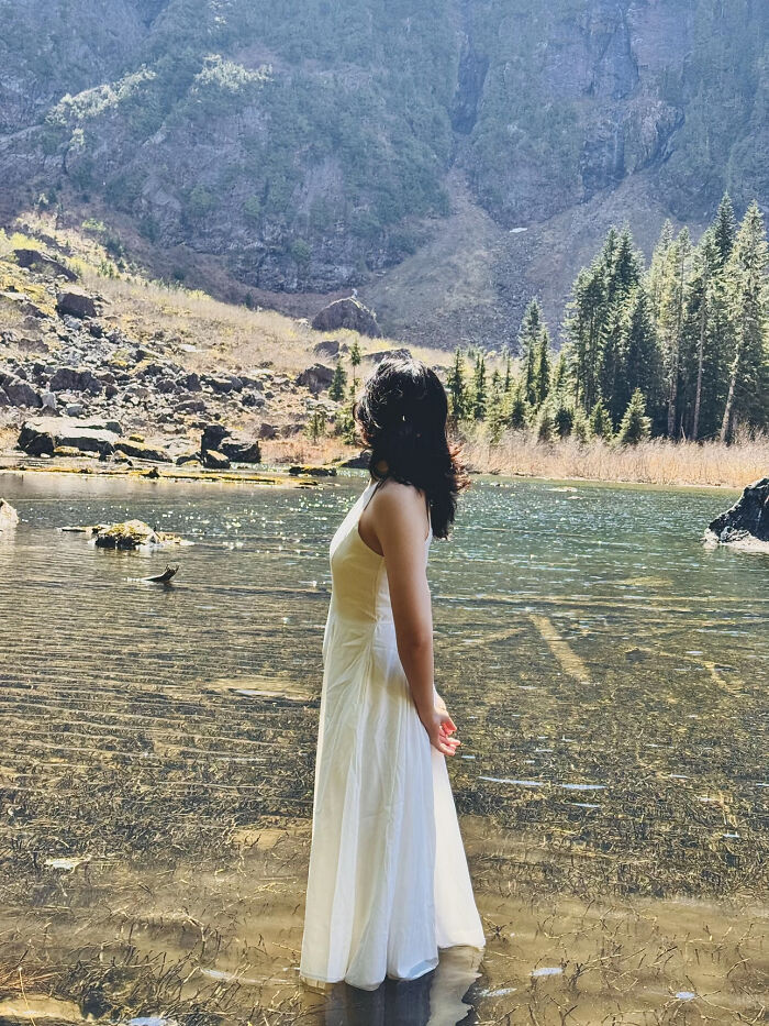 Woman in white dress standing in a lake surrounded by mountains and trees