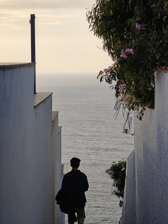 Aesthetic silhouette of person walking between white walls toward ocean view at sunset