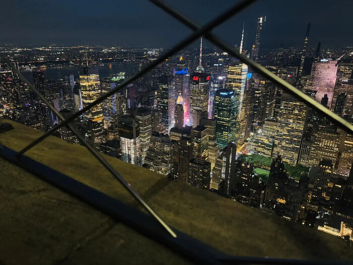 Nighttime city skyline view through fence with bright building lights