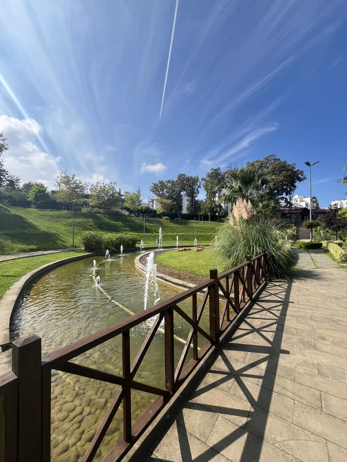 Sunny park pathway alongside curved fountain under blue sky