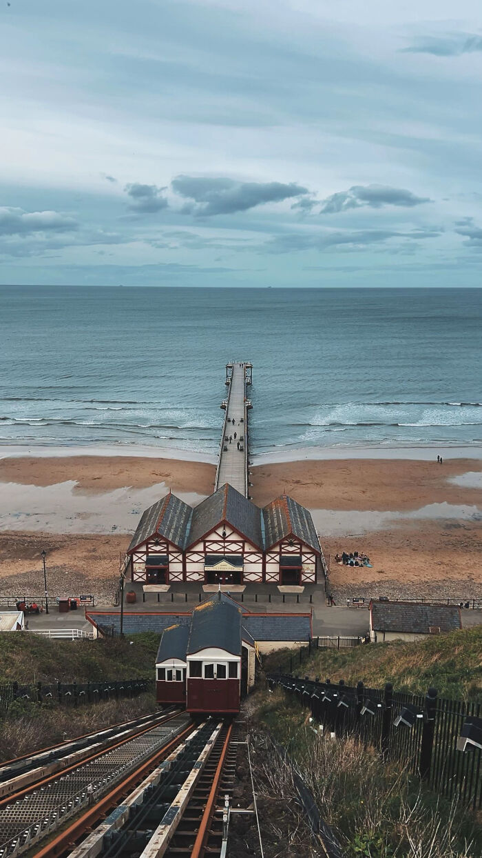 Aesthetic seaside pier with funicular railway and beach under cloudy sky
