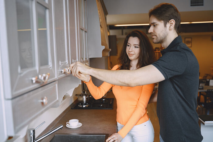 A couple in a kitchen looks at cabinets, deciding on home improvements, a key moment to marry their partner.