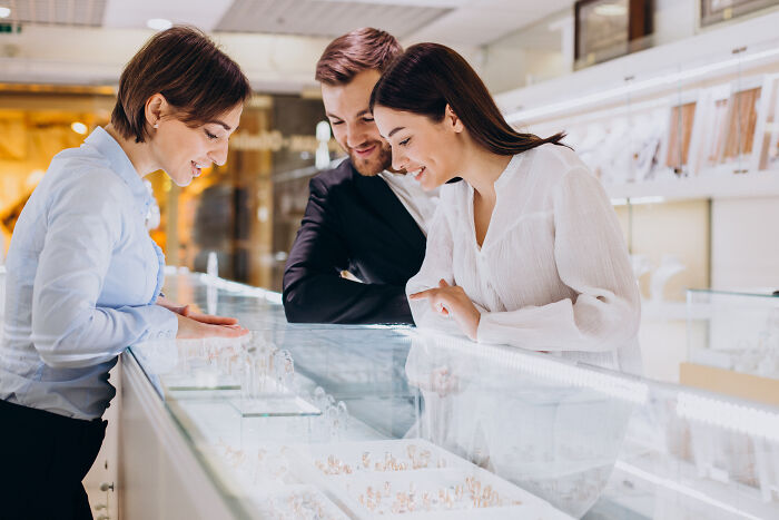 Couple shopping for jewelry, possibly experiencing an awkward situation while making a purchase.