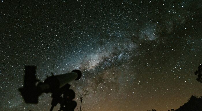 Telescope pointed at starry night sky with the Milky Way, highlighting space observation and astronomy