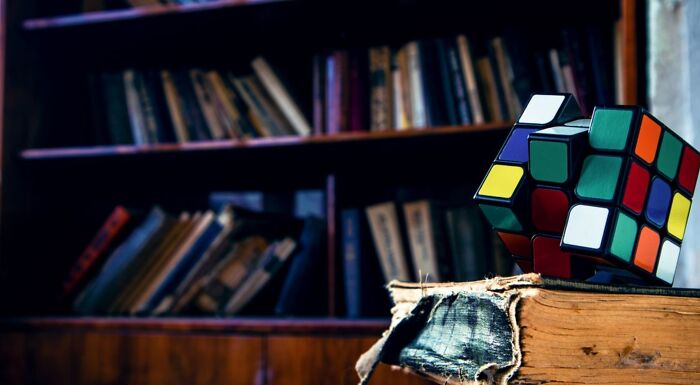 Rubik's Cube on old books with blurred bookshelf background representing IQ challenge Rubik's Cube on old books with blurred bookshelf background representing IQ challenge