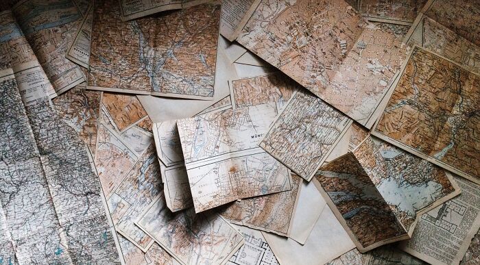 A pile of vintage maps, some folded, showing detailed geographical features, perfect for testing your world knowledge and country questions.