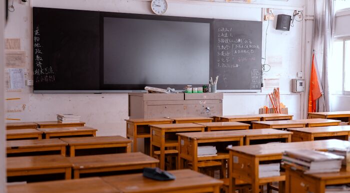 An empty classroom with wooden desks, a blackboard with some writing, and a large screen, symbolizing school questions and a sharp brain.