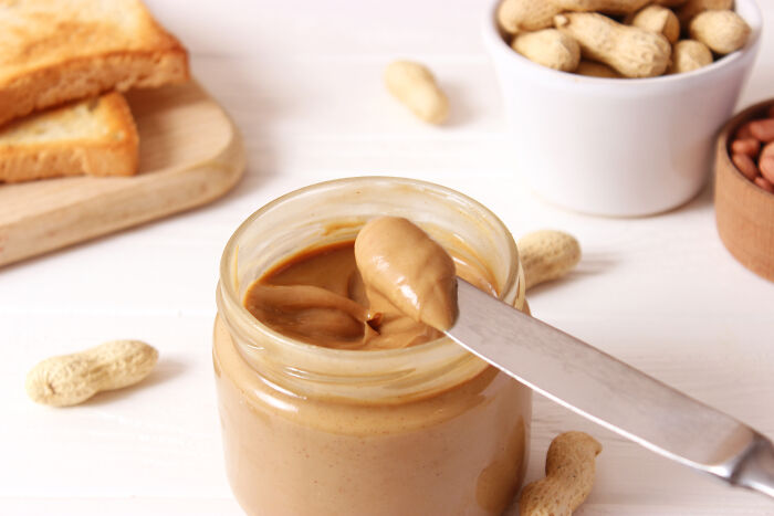 A jar of peanut butter with a knife, alongside toast and peanuts, highlighting weirdly hard to forget facts.