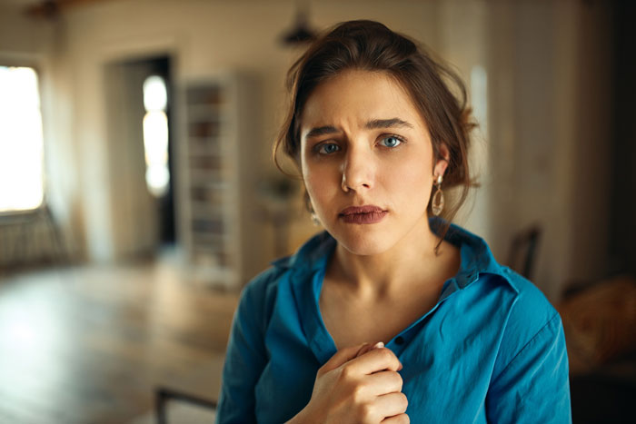 A woman with an unsettled expression, clutching her shirt, reflecting the tension caused by a creepy friend.