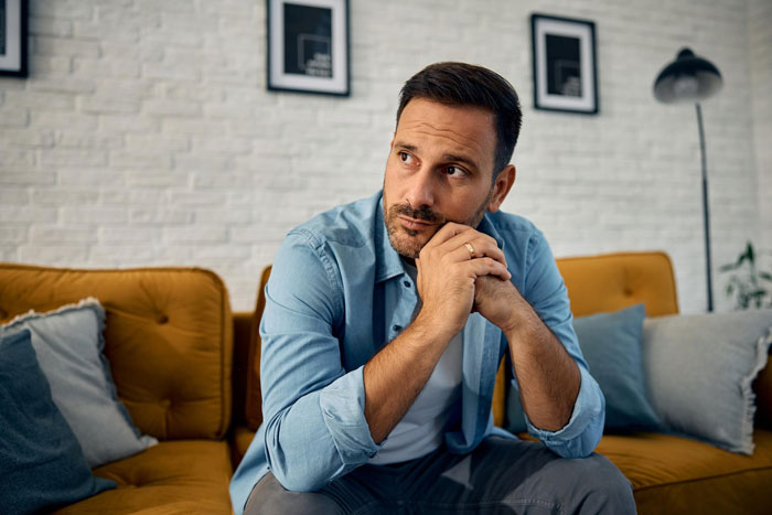 A man looking thoughtful, perhaps worried, on a couch, reflecting on a creepy friend flirting with hubby.