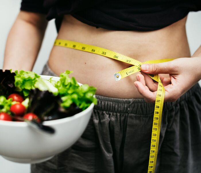 Person measuring waist with tape measure near bowl of salad