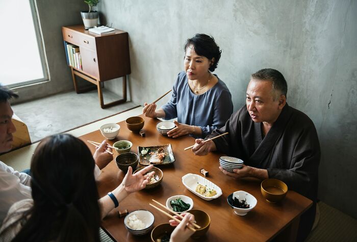 An Asian family eating at a table with chopsticks, demonstrating cultural misunderstandings between locals and foreigners.