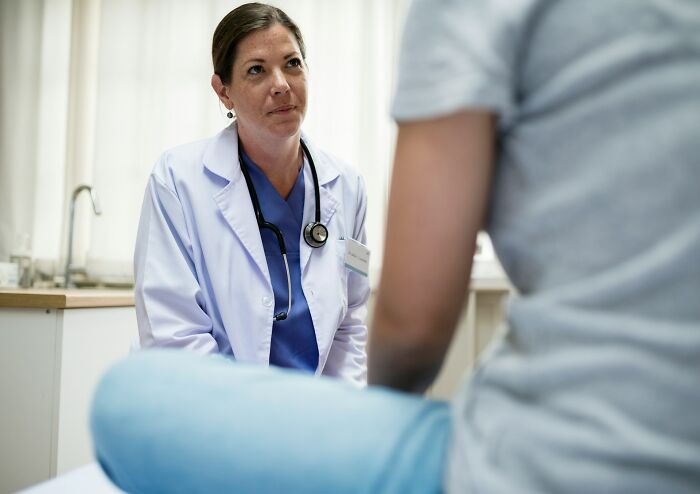 A female doctor in a white coat listening to a patient, discussing health trends and avoiding intense stress and burnout.