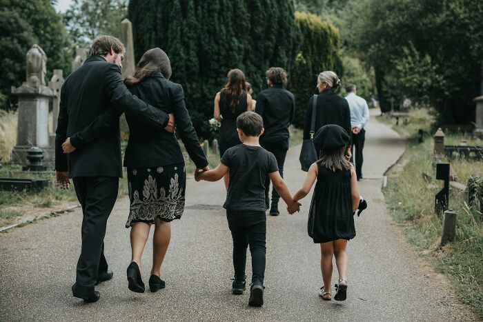 A family dressed in black walking through a cemetery, suggesting the aftermath of exposed double lives.