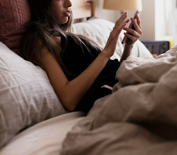 Woman in bed looking shocked at partner's phone screen in hand