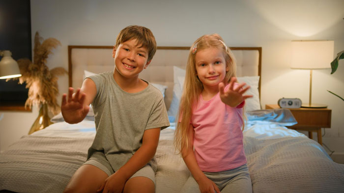 Two kids waving from a bed, possibly the children involved in the dad's secret wedding.