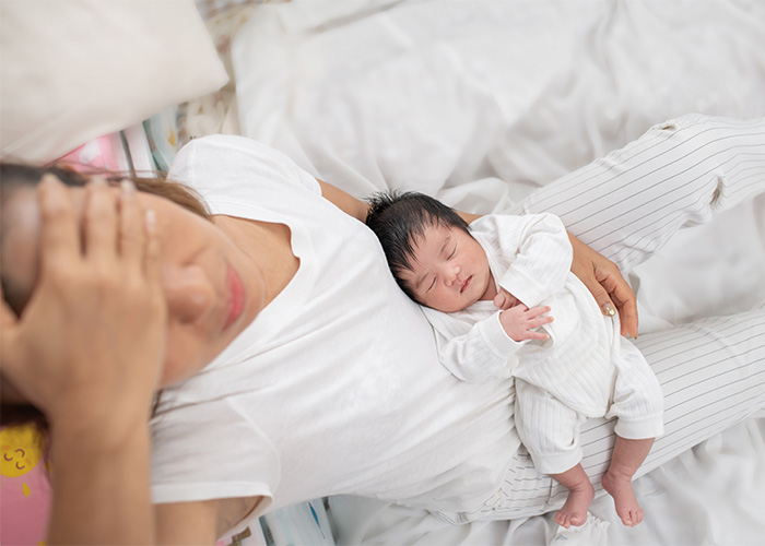 A tired wife lying in bed with a sleeping baby on her chest, highlighting the changes after having kids.