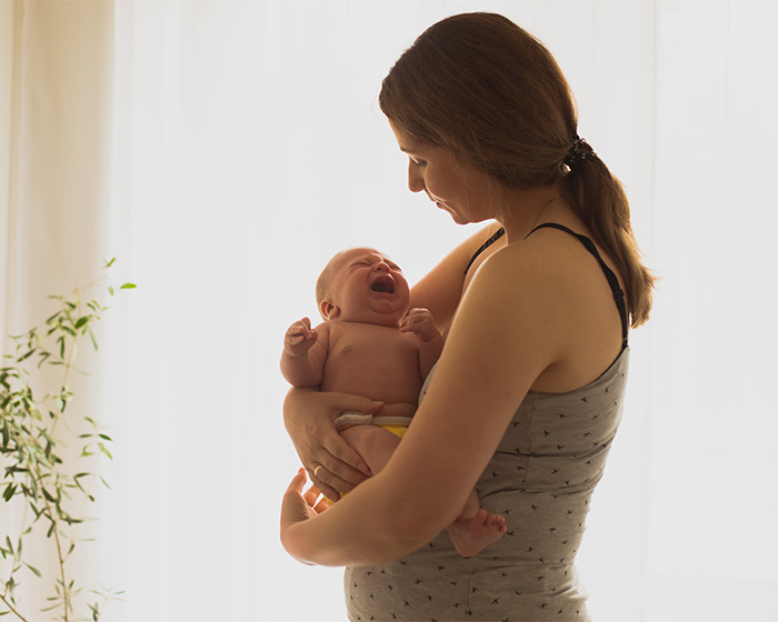 A mother cradling a crying newborn, psychologist asked dads what their wives stopped doing after having kids.