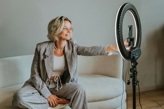 Woman adjusting ring light for video recording at home