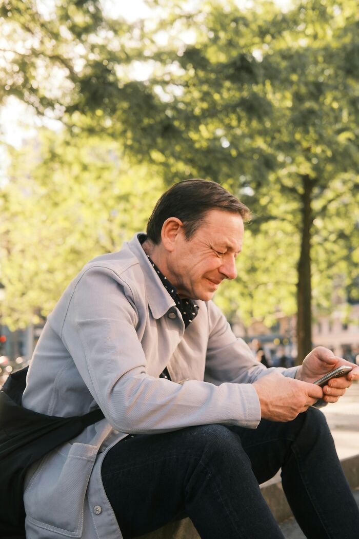 Man outdoors squinting at phone in bright sunlight