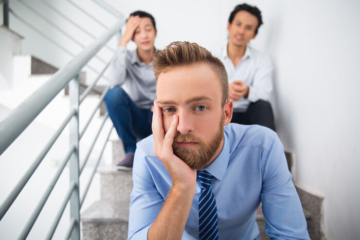 A sad man sitting on stairs with two concerned men in the background, depicting human behavior and emotions.