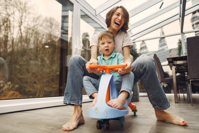 A mother and child laughing while playing with a toy car, illustrating human behavior and happiness.
