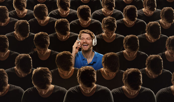 One joyful man in headphones surrounded by many somber, bowed heads, highlighting diverse human behavior.