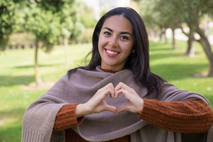 A woman smiling and forming a heart shape with her hands, illustrating positive human behavior and truths.