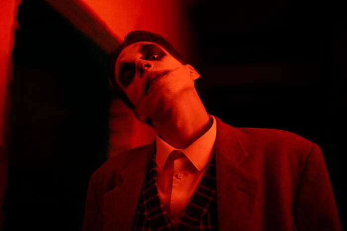 A person in unsettling makeup under red light, a brutal truth about human behavior and darker aspects.
