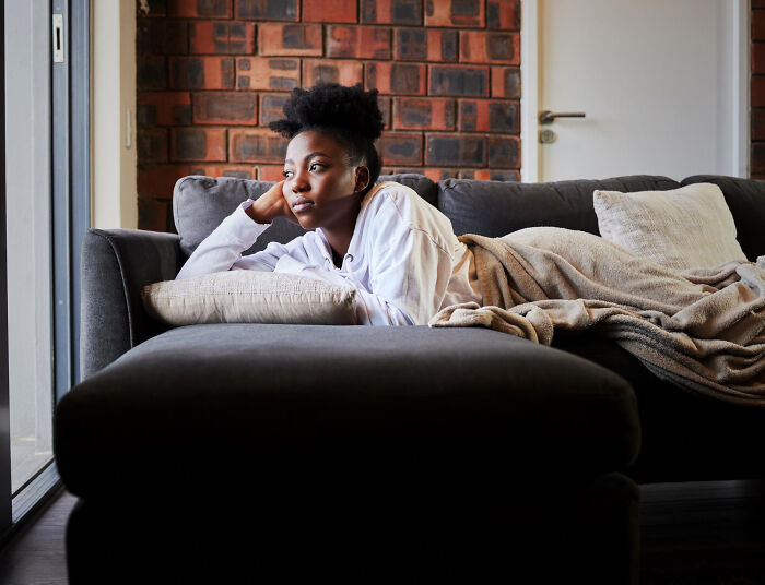 A young woman resting on a sofa, looking contemplative, showcasing human behavior and introspection.