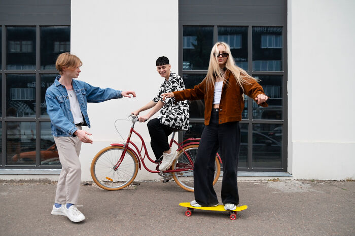 Three friends displaying various human behavior; one on a bicycle, another on a skateboard, and one observing.