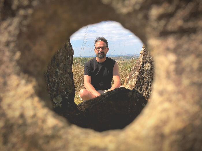 A man meditating outdoors, seen through a rock formation, symbolizing human behavior and mindfulness.