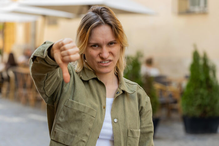 A woman giving a thumbs down, representing negative human behavior or truths that people avoid.