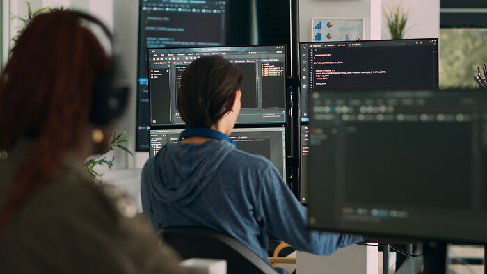 Two programmers working on multiple screens, illustrating AI-safe careers in tech.