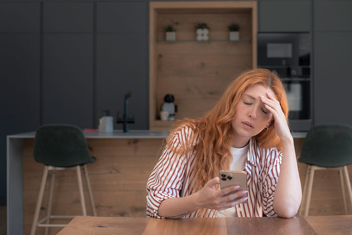 A 28YO woman looking upset, holding a phone, feeling her frugal life is disrespected by parents' actions. A 28YO woman looking upset, holding a phone, feeling her frugal life is disrespected by parents' actions.