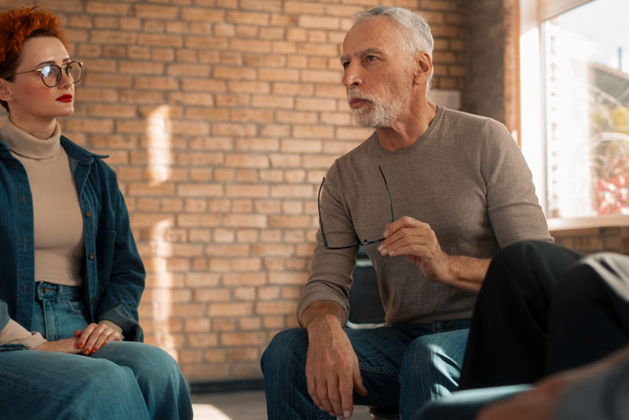 Older man holding glasses talking seriously with younger woman indoors Older man holding glasses talking seriously with younger woman indoors