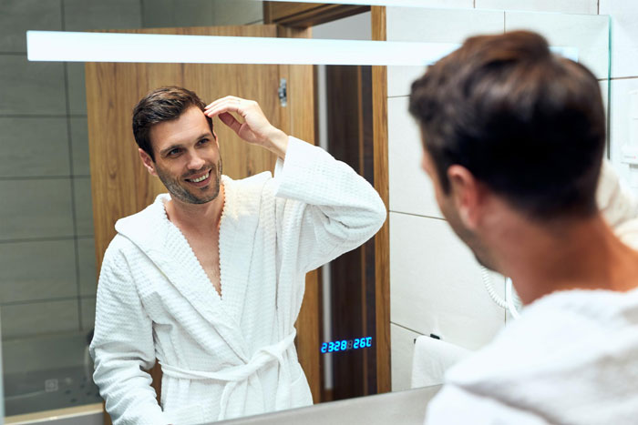 Man in bathrobe smiling at himself in mirror grooming hair Man in bathrobe smiling at himself in mirror grooming hair