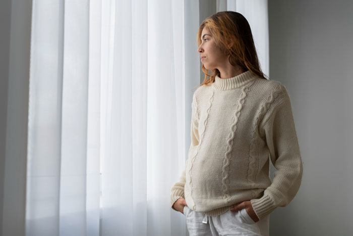 Pregnant woman looking out window feeling contemplative about man ghosting Pregnant woman looking out window feeling contemplative about man ghosting